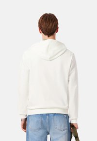Sudadera con capucha blanca hecha de tela suave, con capucha ajustable con cordón, puños y dobladillo acanalados, combinada con jeans de mezclilla azul claro.