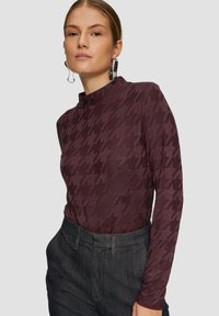 Langhuis-top in diep bordeaux met een houndstooth-patroon, met een neklijnontwerp en een gladde textuur, gecombineerd met donkere broek.