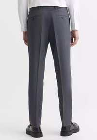 Szare spodnie w prążek o dopasowanym kroju, z dwiema tylnymi kieszeniami i gładkim przodem. Noszone z białą koszulą i czarnymi butami.