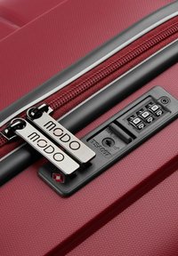 Red hard-shell suitcase with textured surface, dual zippers, branded pulls, and a TSA combination lock. Features black accent around the zipper.