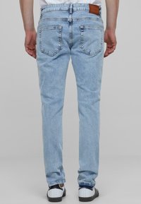 Jean en denim bleu clair à coupe droite, avec deux poches arrière, un accent en cuir à la taille et un léger délavage sur l'ensemble.