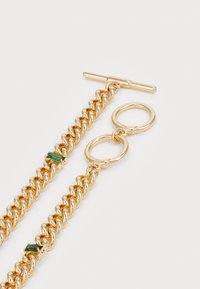 Collana in oro con maglie intrecciate, chiusura a toggle e una pietra verde inserita nel design.
