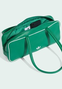 Zelena kožnata torba s bijelim obrubom. Ima dva ručka i zatvara se patentnim zatvaračem na vrhu, s unutarnjim džepom u kojem se nalazi telefon.