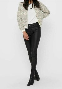 Veste bomber fleurie couleur crème, poignets élastiques, portée sur une chemise blanche, associée à un pantalon en cuir noir cintré et des bottines pointues.