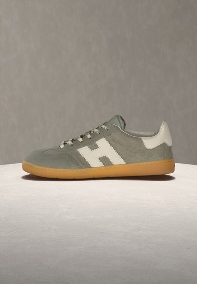 Γκρι δερμάτινο αθλητικό παπούτσι από σουέτ με λευκή φτέρνα, λευκό λογότυπο "H" στο πλάι, μπεζ κορδόνια και ελαφρώς καφέ λαστιχένια σόλα πάνω σε ανοιχτόχρωμη επιφάνεια.