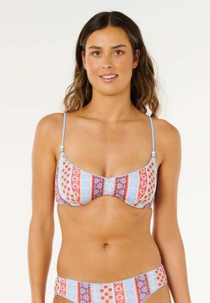 Kobieta z długimi brązowymi włosami, ubrana w bikini z wzorem, z czerwonymi, niebieskimi i białymi pionowymi paskami oraz kwiatowymi motywami.