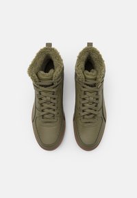 Pár olivově zelených vysokých tenisek s ovčí podsadou, hnědými podrážkami a tkaničkami, z pohledu shora na bílém pozadí.