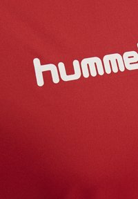 Roter Stoff mit teilweise weiß gedrucktem "hummel" Markenlogo in abgerundeten Kleinbuchstaben.