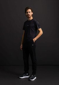 Zwarte sportieve t-shirt met korte mouwen en logo, gecombineerd met zwarte joggingsbroeken en zwarte sneakers. Glad materiaal met een aansluitend ontwerp.