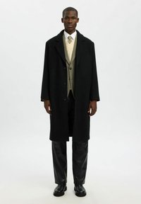 Mustad must coat, millel lõdva lõike, sälk-lapellide ja nööbiga sulgemisega, kihtide all on hundi-hamstriga vest ja mustad püksid.