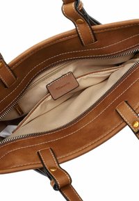 Interno di una borsa a tracolla in suede marrone, con fodera beige, numerose tasche con zip e un'etichetta in pelle del marchio. Dettagli di cucitura a contrasto visibili.