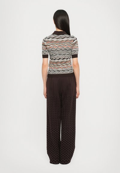 Knitted top with wavy pattern in brown, cream, and rust colors. Paired with wide-leg trousers featuring a zigzag texture in dark brown.
