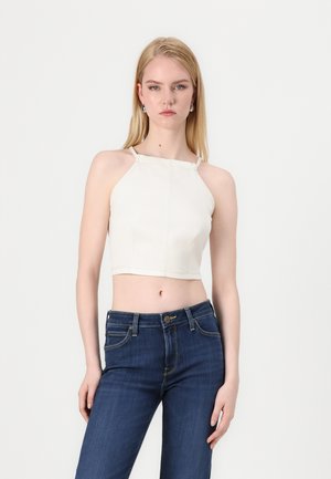 Kremfarget cropped topp med tynne stropper og en fitted design. Et par mørke denimjeans med synlig søm og klassiske lommer.