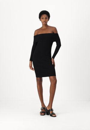 Abito nero a coste off-shoulder con maniche lunghe, forma aderente, lunghezza al ginocchio. Abbinato a sandali neri con tacco che presentano dettagli dorati.