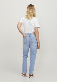 Jeans azzurri chiari a vita alta con una vestibilità rilassata, due tasche posteriori e un'etichetta marrone in vita, abbinati a una maglietta bianca.