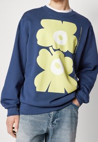 Námořnická mikina s velkými žlutými a bílými květinovými grafikami, kulatým výstřihem, dlouhými rukávy, z bavlněného materiálu a s žebrovanými manžetami.