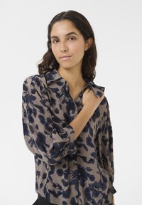 Cămașă cu mânecă lungă dintr-un material maro, cu un model abstract albastru închis, având guler, închidere cu nasturi și detalii plisate la manșete.