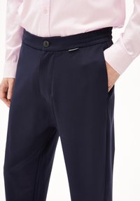 Marineblauwe broek met een gladde textuur en elastische tailleband, voorzien van een knoopsluiting aan de voorkant en zijzakken.