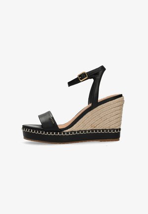 Czarna sandałka na koturnie z paskiem wokół kostki, złotą klamrą, plecioną platformą z juty oraz przeszyciami wzdłuż podeszwy.