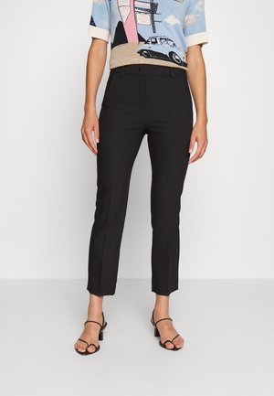 Kvinde iført sorte cropped slim-fit bukser, blå grafisk kortærmet top og sorte remsandaler med hæl.