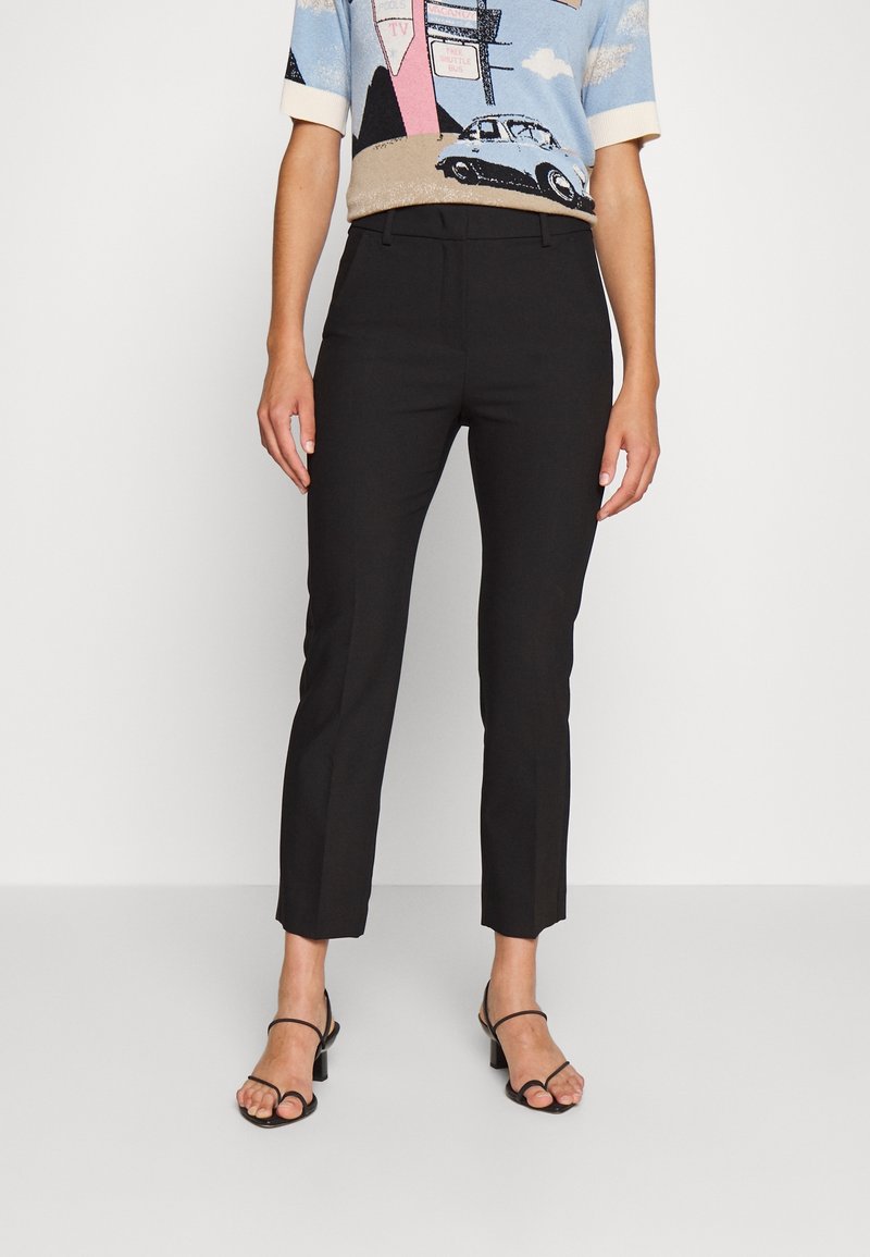 Femme portant un pantalon noir court slim, un haut bleu à manches courtes avec un motif graphique, et des sandales à talons noires à lanières.