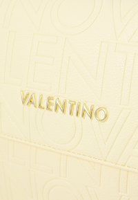 Borsa in pelle color crema con branding impresso e dettagli metallici dorati, caratterizzata da una superficie liscia e bordi arrotondati.