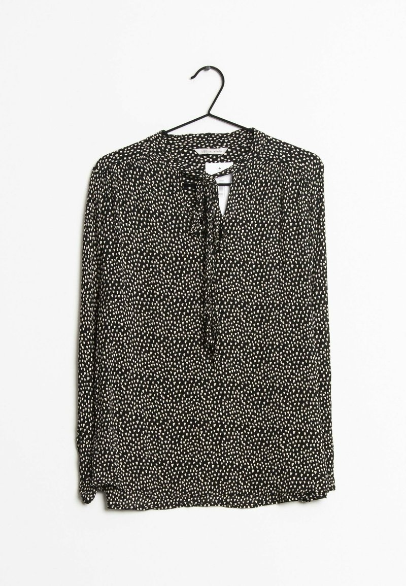 Zwarte blouse met lange mouwen en kleine witte hartjespatronen, met een striknek, hangend aan een zwarte hanger tegen een witte achtergrond.