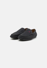 Mocassins en suède noir avec un bout rond, des coutures décoratives et un accent rouge et blanc près du côté. Semelle en caoutchouc pour une meilleure adhérence.