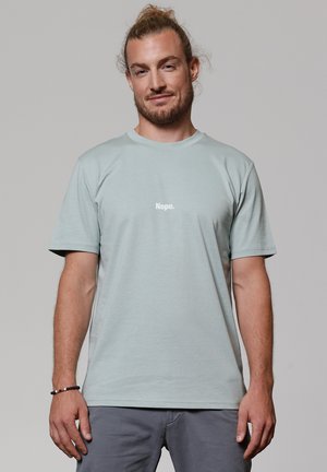 T-shirt en coton bleu clair à manches courtes, avec le texte « Nope. » en blanc. Design simple, encolure ras du cou, coupe décontractée.