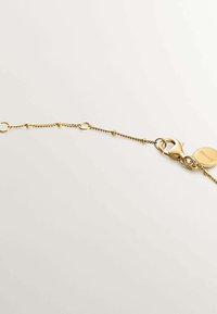 Pulsera de oro con un diseño de cadena delicada, que presenta un cierre de langosta y un charm redondo con detalles grabados. Textura suave y acabado brillante.