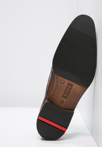 Sole di scarpa elegante in pelle marrone, con una base in gomma texturizzata, logo del marchio impresso e una striscia rossa vicino al tacco.