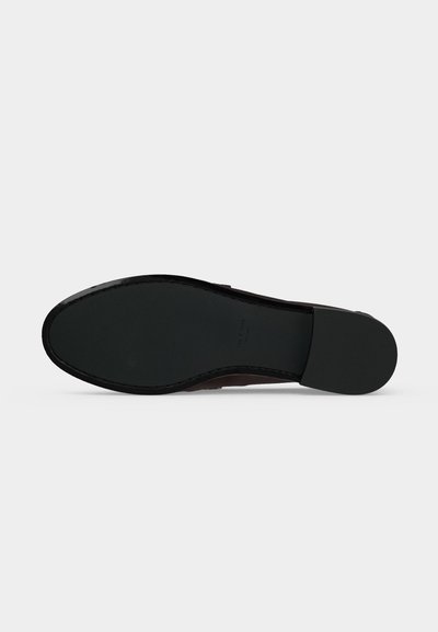 Semelle d'une chaussure habillée en cuir noir avec une semelle lisse et un talon bas empilé visible sur un fond clair.