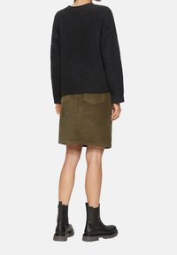 Schwarzer, strukturierter Pullover, grüne Cord-Rock mit Taschen und schwarze Stiefeletten mit dicker Sohle. Rückansicht des Outfits.