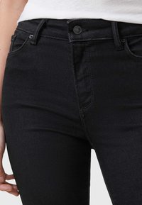 Jean en denim noir à taille haute, avec un design à cinq poches et une fermeture à bouton sur le devant. Texture lisse et détails de couture minimalistes.