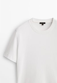 T-shirt bianco in cotone con maniche corte, scollatura rotonda e una texture liscia e semplice. Etichetta visibile sulla parte posteriore del collo.