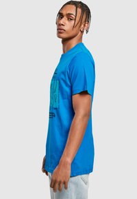 Lysblå bomulds T-shirt med korte ærmer, med et grafisk print på forsiden med abstrakte designs og tekst i sort.