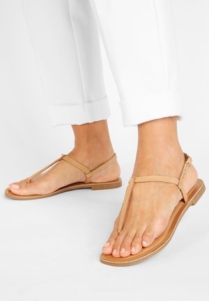 Jasnobrązowe skórzane sandały z paskiem na palce i zapięciem na kostkę, płaską podeszwą i minimalistycznym designem. Paski mają subtelne detale w postaci przeszyć.