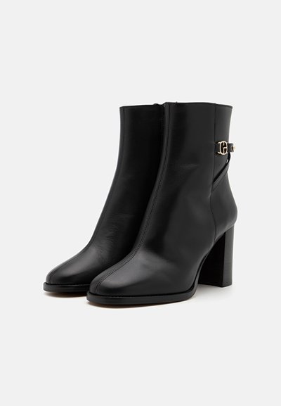 Bottines noires en cuir avec un bout carré, un talon bloc haut, une fermeture éclair sur le côté et des accents dorés près de la cheville. Texture lisse.