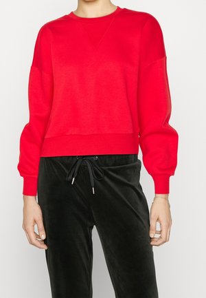 Red cropped sweatshirt with a crew neckline and long, slightly puffed sleeves. Paired with black velvet joggers featuring a drawstring.