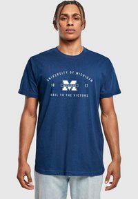 Námořnická modrá bavlněná tričko s textem "University of Michigan" a bílým logem "M", s uvolněným střihem a krátkými rukávy.