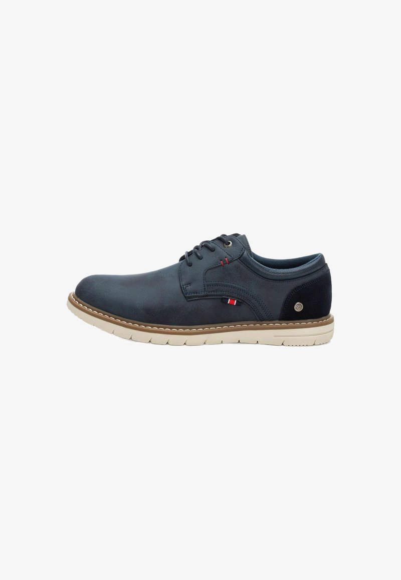 Zapatos de cuero azul oscuro para hombres con cordones, suela beige, costura elevada y detalle de logo lateral. Textura suave con un diseño de punta redondeada.