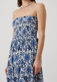 Bezramenné květinové maxi šaty s gumičkovým korpusem v modro-bílých vzorech, s vrstveným designem a lehkým materiálem.