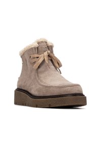 Botín de ante beige con suela de goma texturizada, diseño con cordones y un cálido collar de piel sintética de color crema.