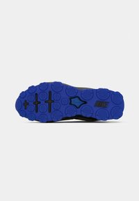 Črna podplat športnih copat z podrobnim modrim gumijastim vzorcem, ki vključuje okrogle oprijemalne točke in izstopajoči Nike logotip v črni barvi.