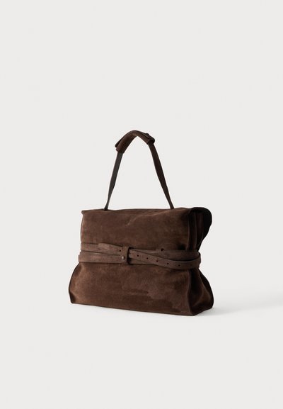 Καφέ τσάντα από σουέντ με μία κορυφαία λαβή και λεπτομέρεια ζώνης που τυλίγεται γύρω, σε μονόχρωμο φόντο.