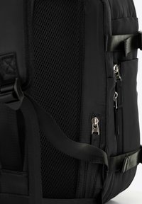 Zaino nero con pannello in rete testurizzato, numerosi zipp e spallacci in nylon. Design compatto con dettagli lisci e forma strutturata.