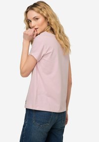 Camiseta de algodón rosa claro con mangas cortas y un escote redondo, combinada con jeans de mezclilla azul. Presenta un diseño simple y casual.