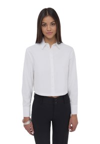 Camicia bianca tagliata con maniche lunghe, colletto e tessuto morbido; abbinata a pantaloni neri attillati con chiusura a doppio bottone.