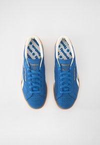 Tenisi bleumarin din suede, cu accente albe, vârf rotund, design cu șireturi, perforații circulare pe zona vârfului și talpă din cauciuc de tip gumă. Branding Reebok vizibil.