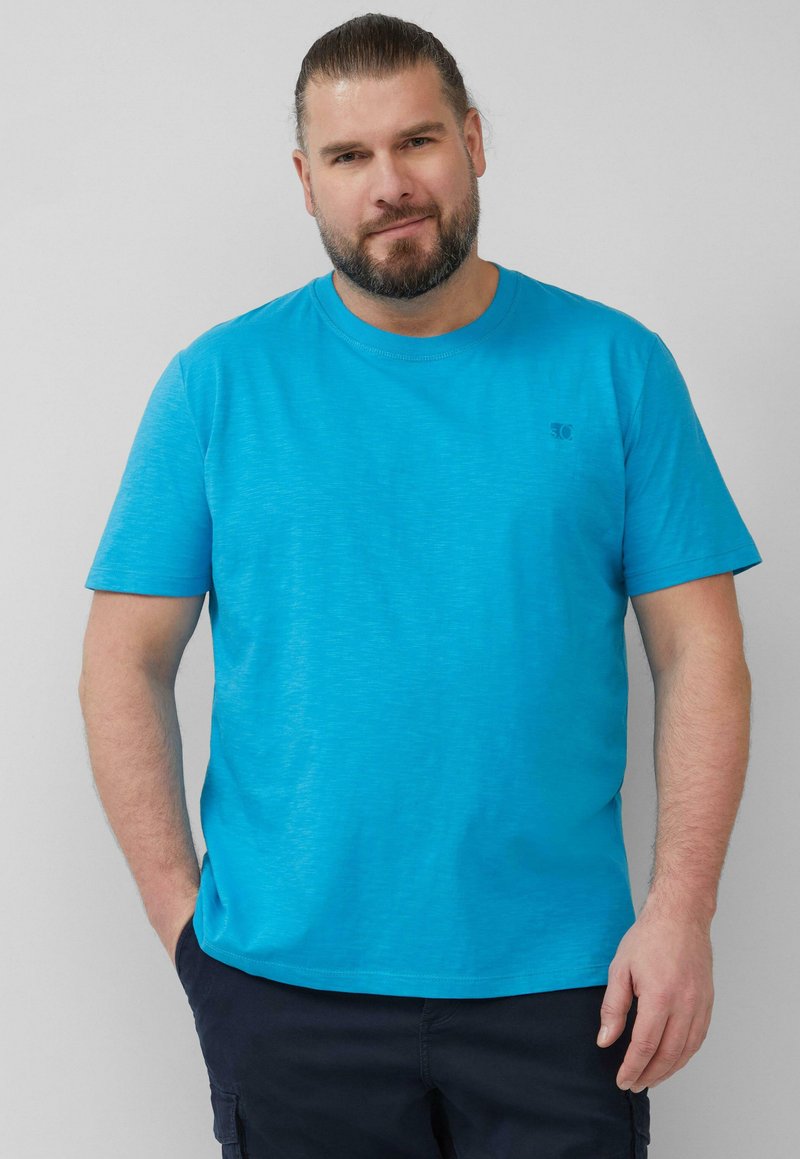 Türkises T-Shirt mit kurzen Ärmeln aus einem weichen, leichten Stoff mit subtiler Textur, das ein kleines Logo auf der Brust trägt.